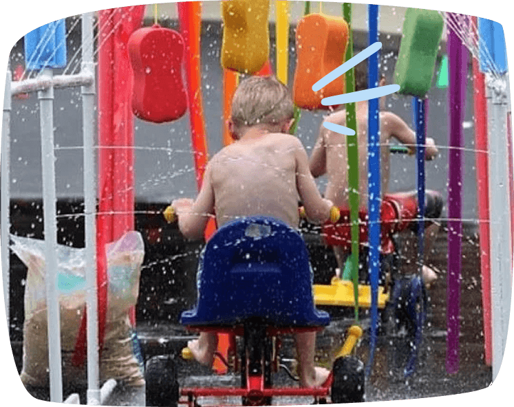 kid on trycicle under sprinklers