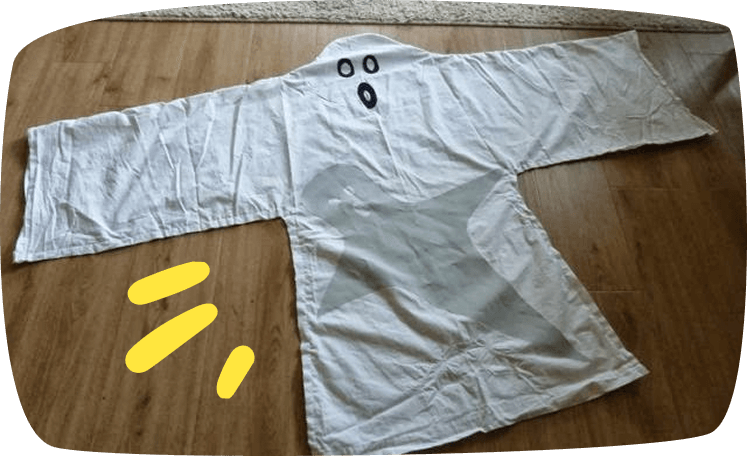 Sehelai kain atau jubah putih diletakkan di lantai kayu dengan bulatan hitam dilukis untuk menyerupai wajah hantu, seperti kostum hantu Halloween buatan sendiri.