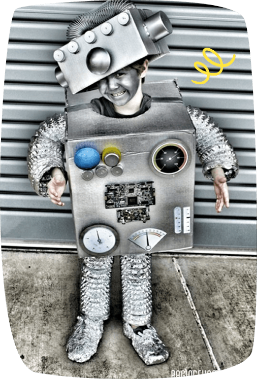 Seorang kanak-kanak berpakaian kostum robot buatan tangan daripada kotak karton, aluminium foil, dan pelbagai alat kecil, tersenyum lebar sambil bergaya di hadapan latar belakang peneduh logam.